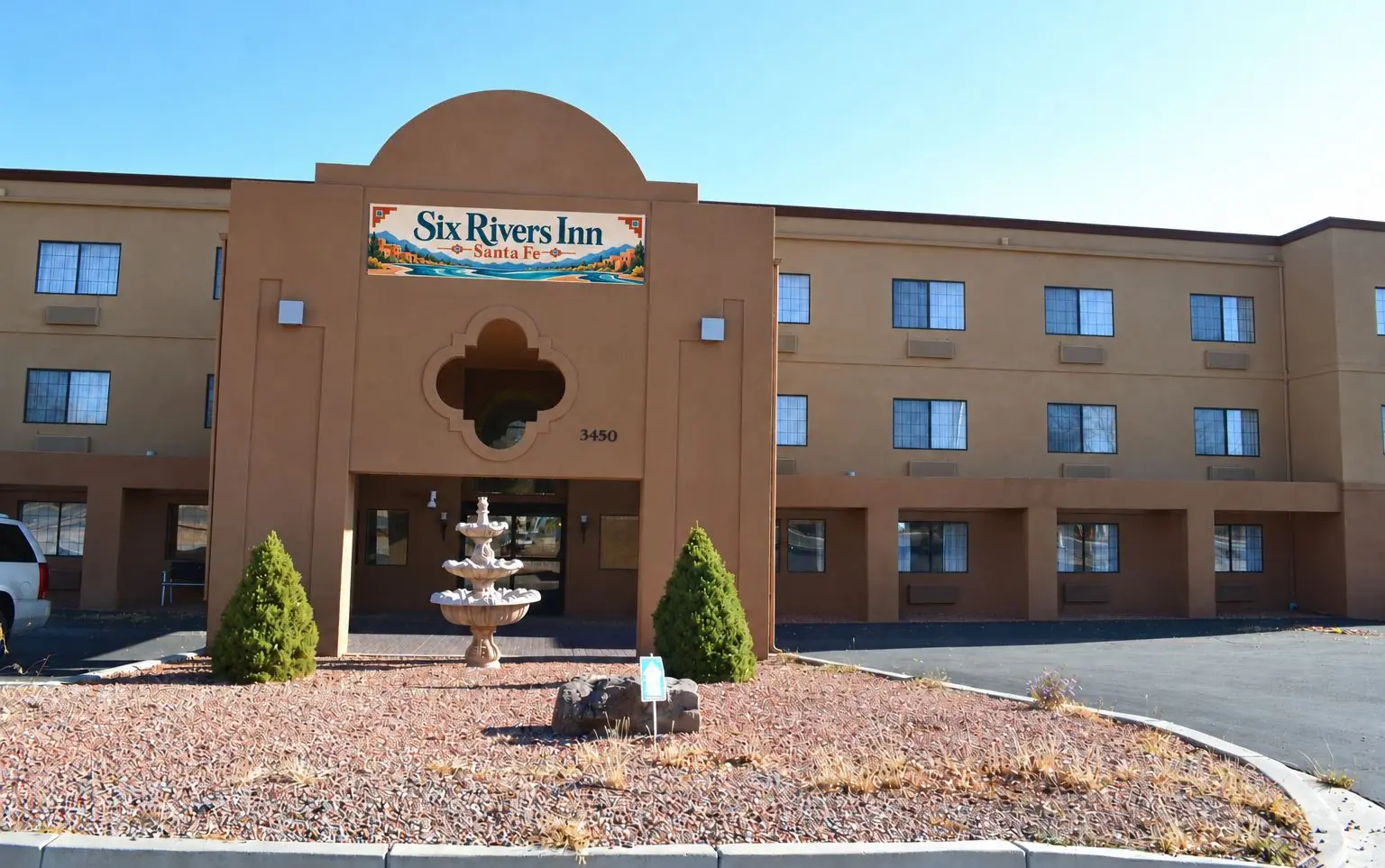 Six Rivers Inn Santa Fe by day: adobe-style entrance tower with the new sign, fountain and three-story building at 3450 Cerrillos Road